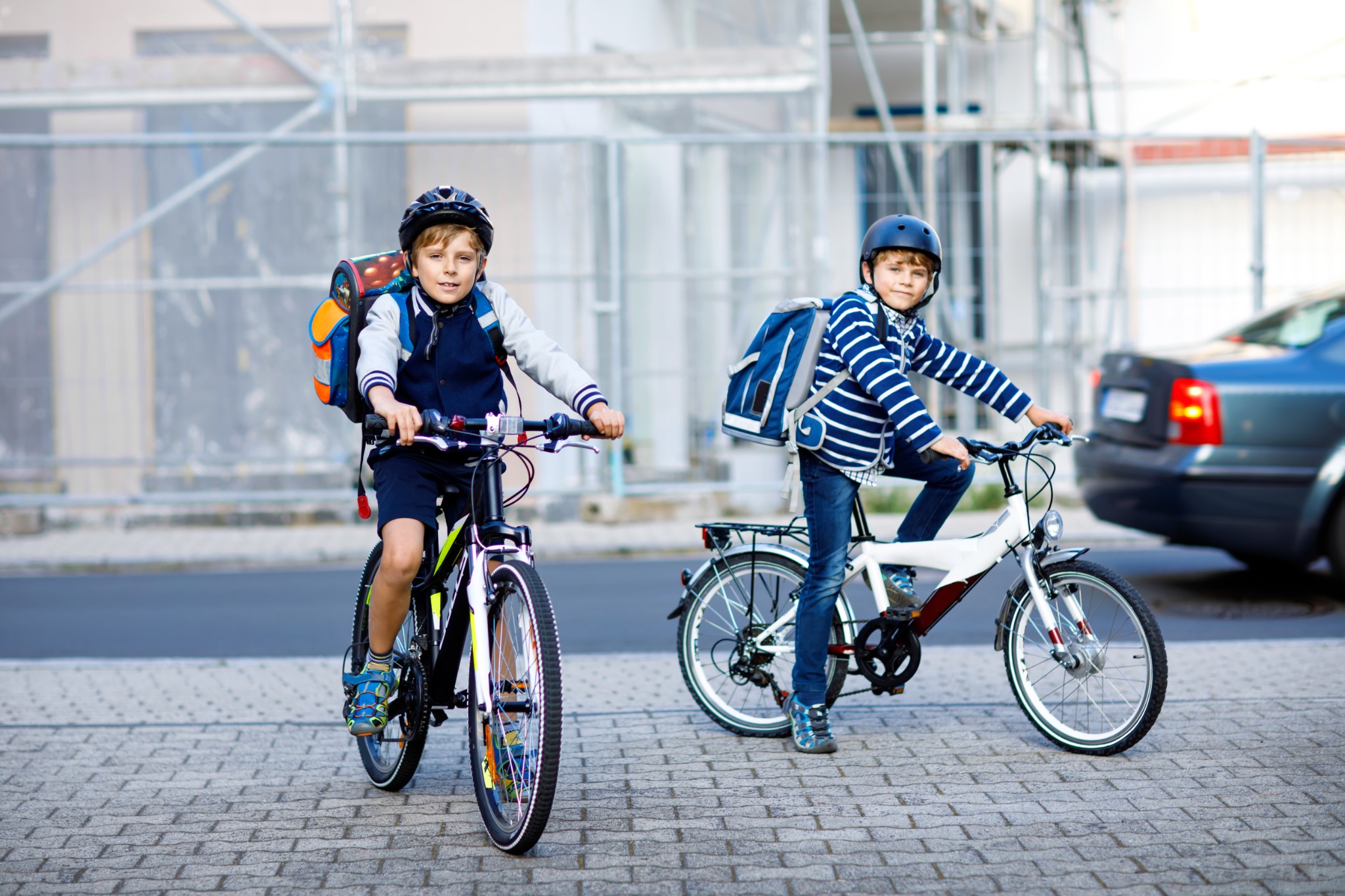 Two children wearing helmets while riding bicycles near a roadway